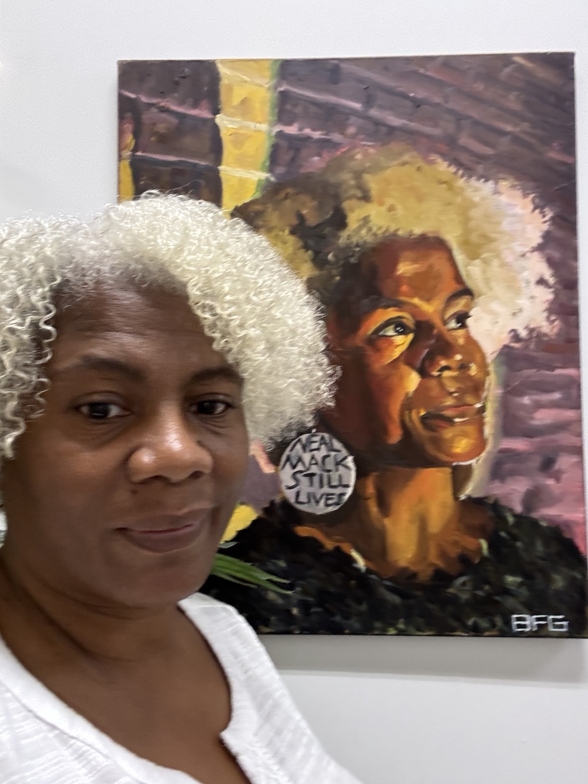 Cariol Horne beside a painted portrait while wearing earrings that read Neal Mack Still Lives